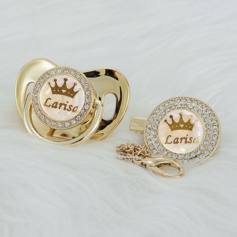 Gold Custom Personalized Pacifiers for Reborn Baby Dolls and Newborn Babies with names, crown, pearlescent backgrounds, and bling. Comes with a pacifier clip in gold.