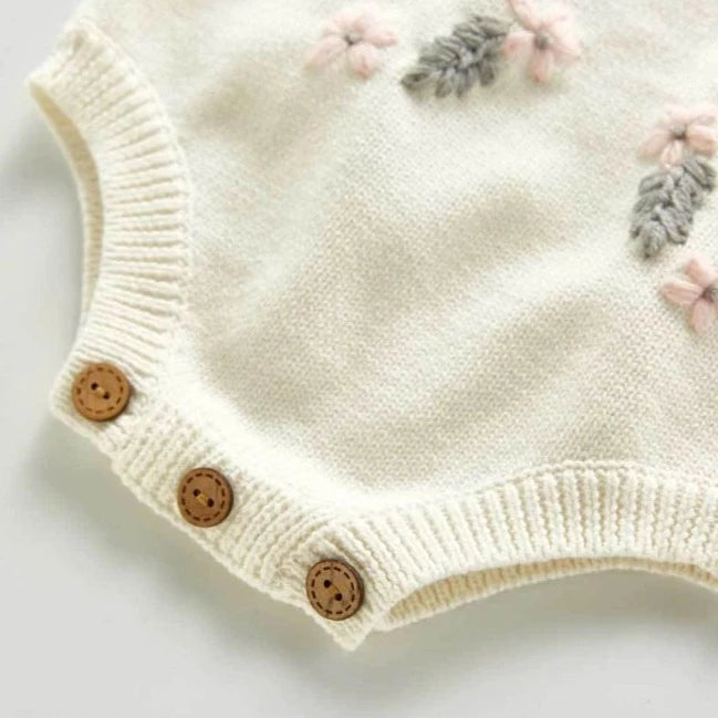 Creamy white knitted overall style onesie with buttons on the overall straps. Has beautiful pink and grey floral embroidery on the belly and buttons on the crotch. Made for newborn baby girls to 3 years old and reborn dolls.