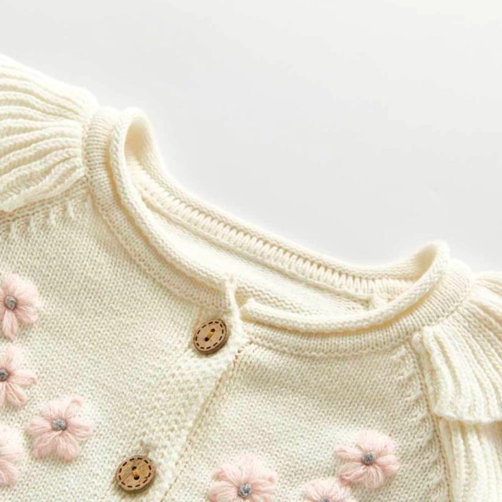 Close-up of the collar / neckline of hte Creamy white knitted cardigan with frilly sleeves, long-sleeves, and buttons down the centre. Has beautiful pink and grey floral embroidery on the chest. Made for newborn baby girls to 3 years old and reborn dolls.