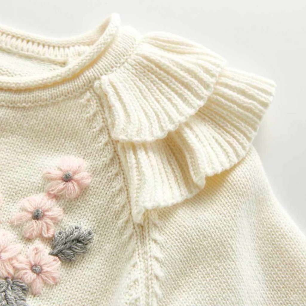 Close up of the frilly sleeves on the Creamy white knitted cardigan with frilly sleeves, long-sleeves, and buttons down the centre. Has beautiful pink and grey floral embroidery on the chest. Made for newborn baby girls to 3 years old and reborn dolls.