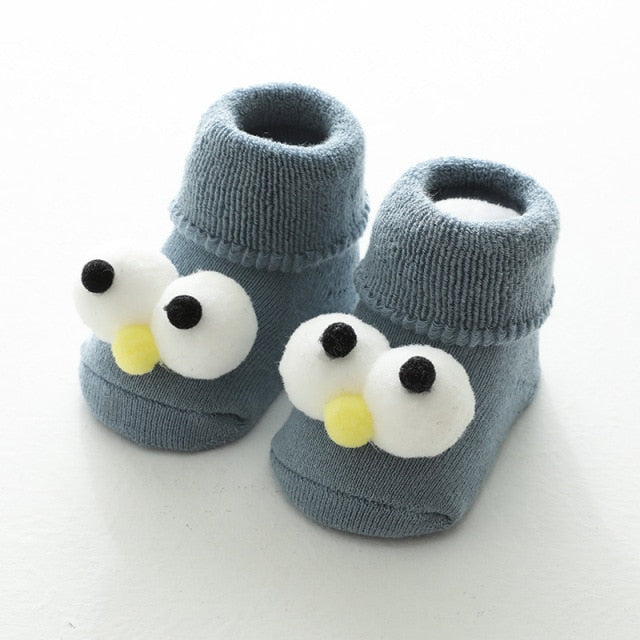 Blue 0-12 month baby socks with puff ball eyes and a puff ball nose, that looks like cookie monster from sesame street for reborn dolls or cuddle babies.