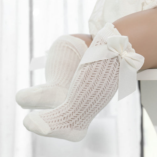 Off white knee-high cable knit socks with bow on the top and ruffle detail near the knee.