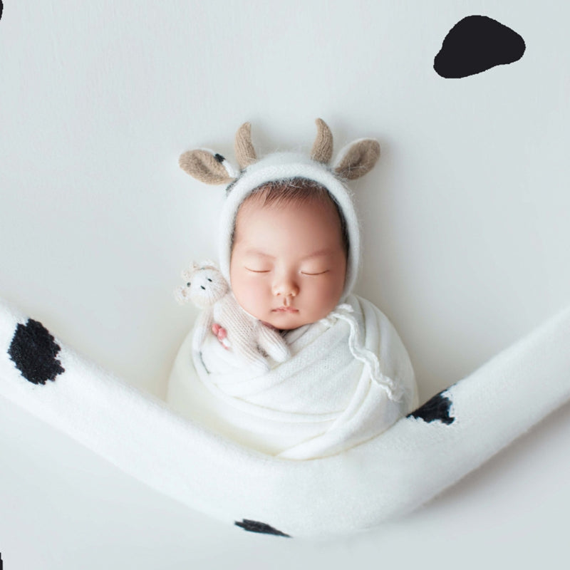 Newborn baby wearing black and white knitted crochet cow hat and matching cow stuffie for reborn dolls, newborn photography, reborn photoshoots, and cuddle babies.